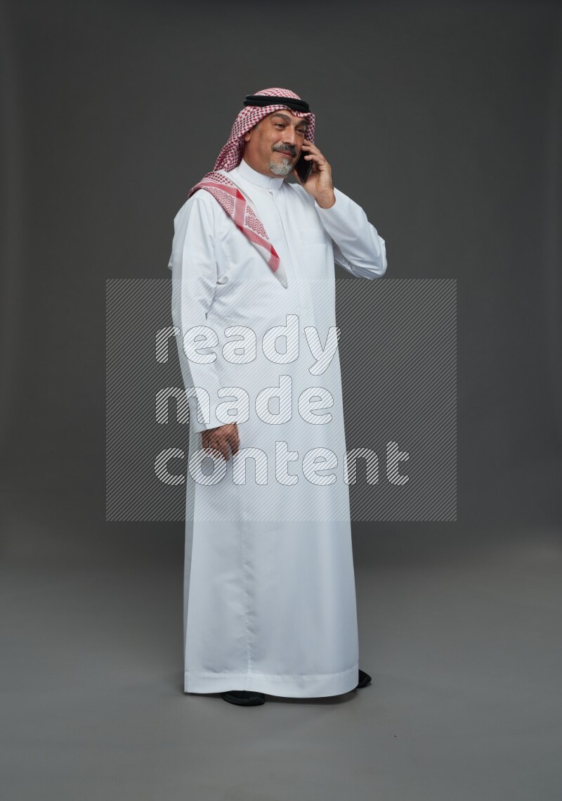 Saudi man with shomag Standing talking on phone on gray background