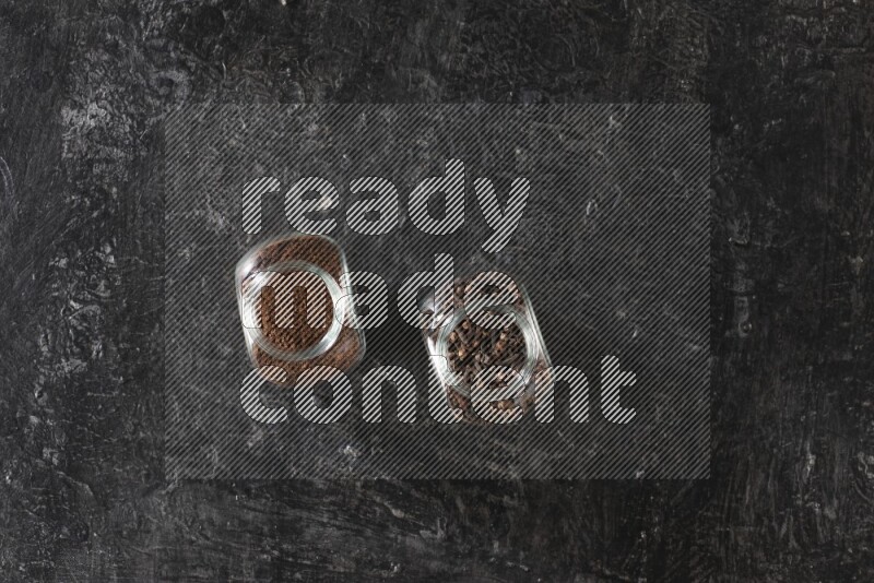 Glass spice jars full of cloves and cloves powder on textured black flooring