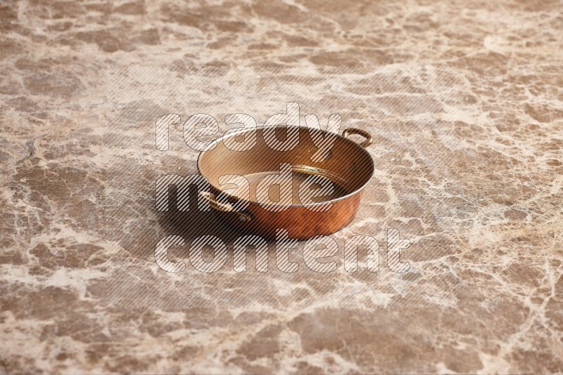 A small copper pan on beige marble background