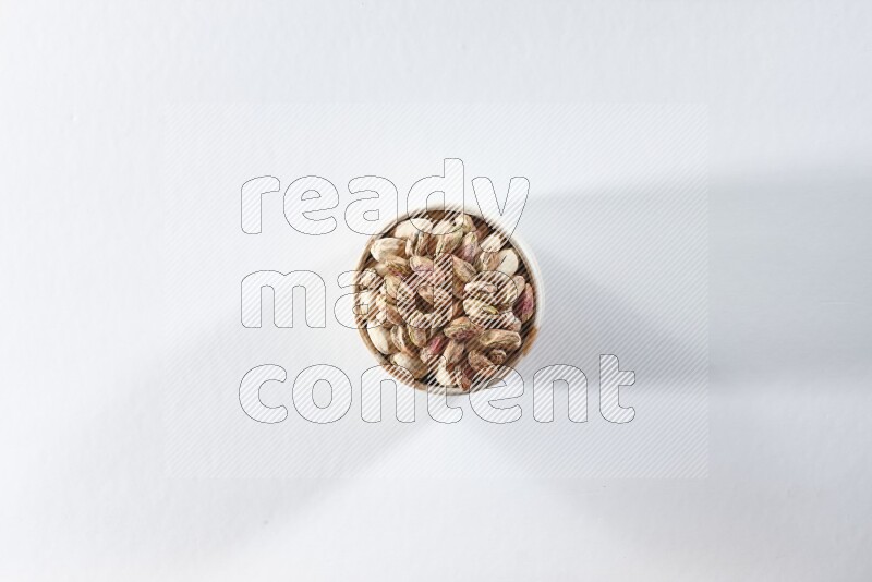A beige ceramic bowl full of peeled pistachios on a white background in different angles