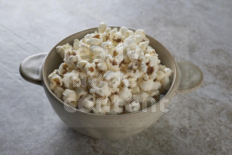 popcorn in a off-white handheld ceramic bowl on a grey textured countertop