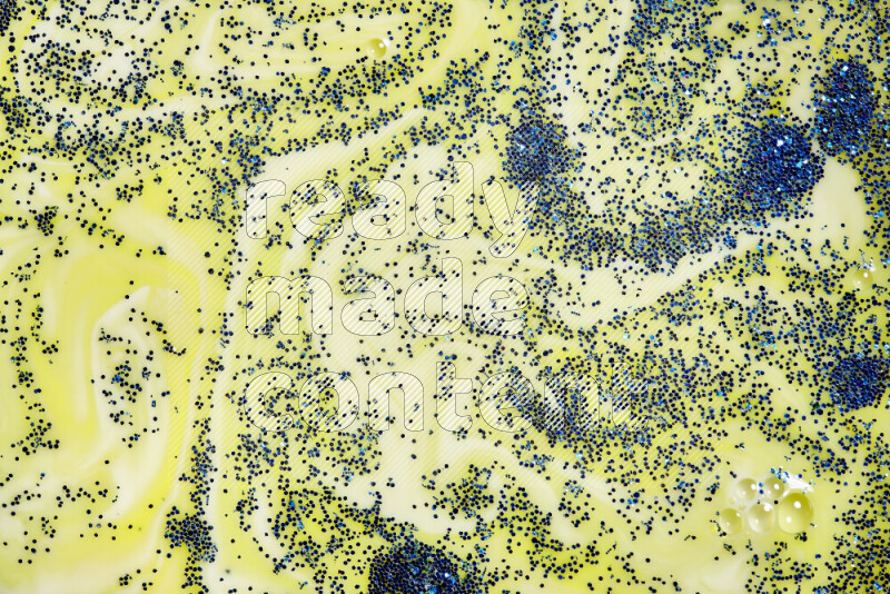 A close-up of sparkling blue glitter scattered on swirling yellow background