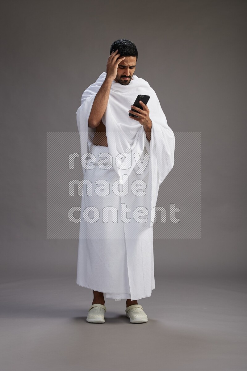 A man wearing Ehram Standing texting on phone on gray background