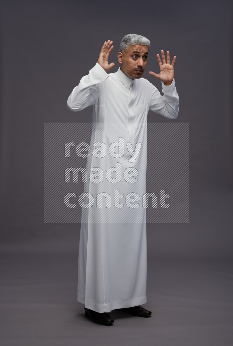 Saudi man wearing thob standing hands behind head on gray background