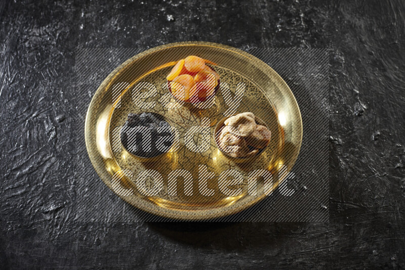 Dried fruits in metal bowls on a tray in a dark setup