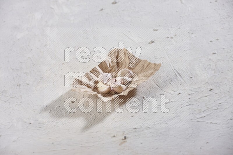A crumpled piece of paper full of garlic cloves placed on a textured white flooring