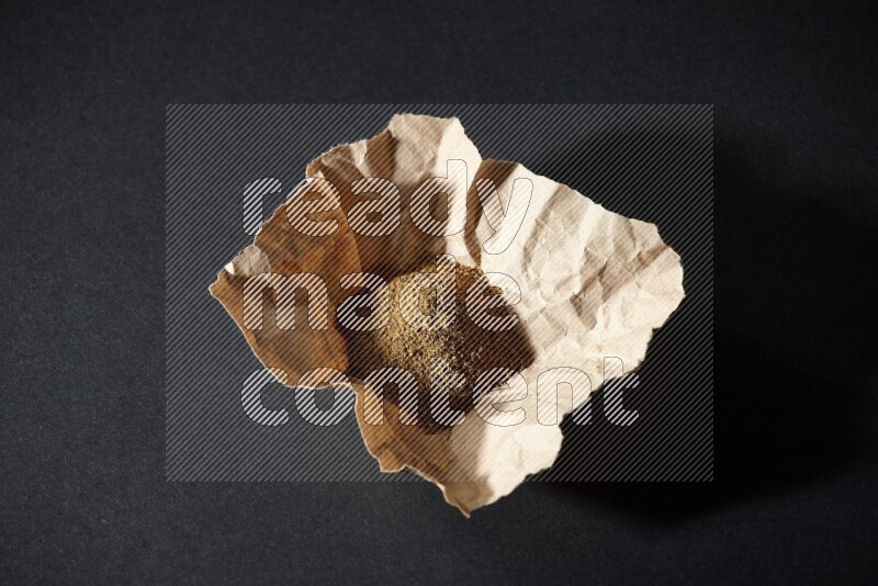 Cumin powder in a crumpled piece of paper on black flooring