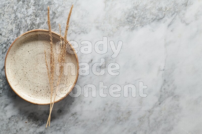 Wheat stalks on multicolored pottery plate on grey marble background