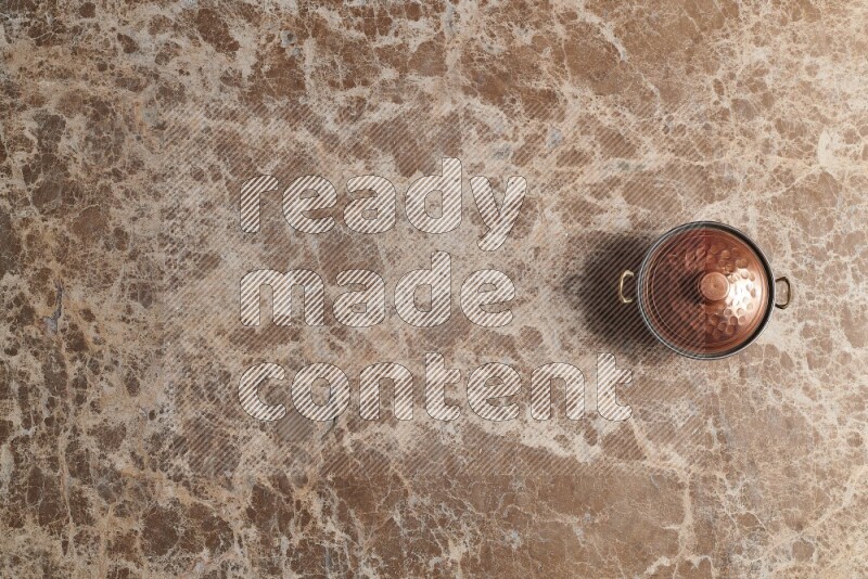 A small copper pot on beige marble background