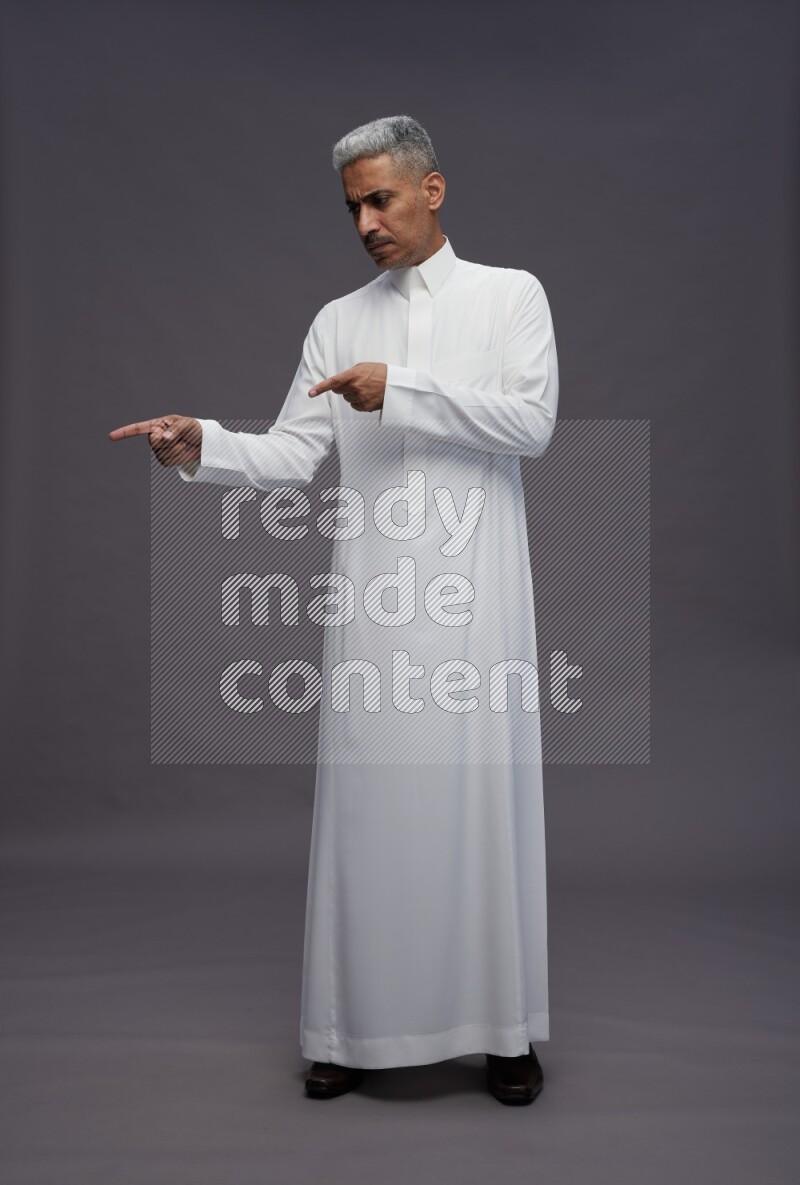 Saudi man wearing thob standing interacting with the camera on gray background