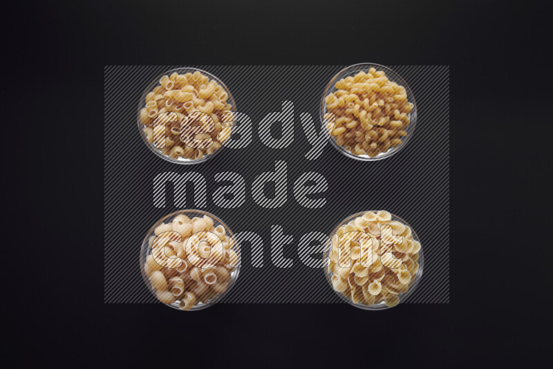 Different pasta types in glass bowls on black background