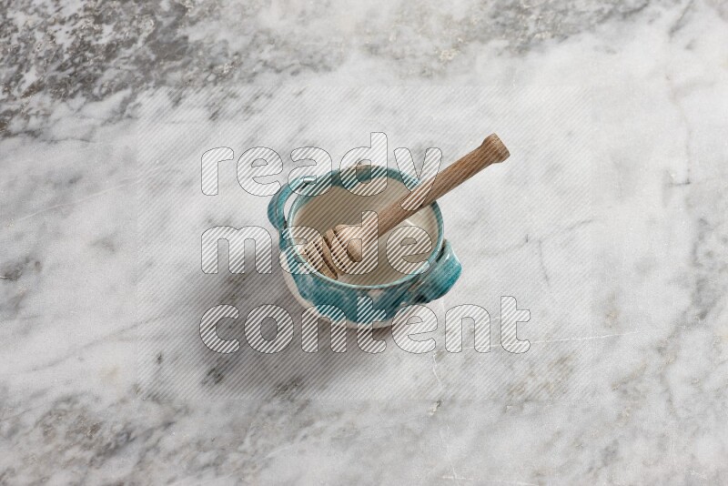 Multicolored pottery bowl with wooden honey dipper in it on grey marble background