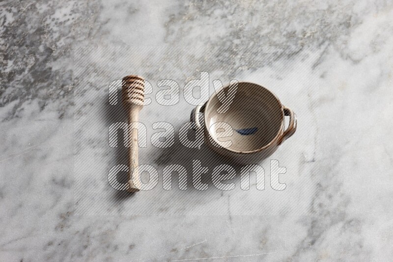 Multicolored pottery bowl with wooden honey dipper on the side on grey marble background