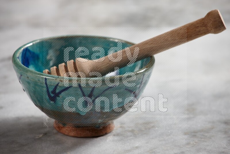 Decorative pottery bowl with wooden honey dipper in it on grey marble background
