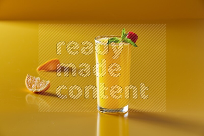 glass of orange juice with berry & mint on yellow background