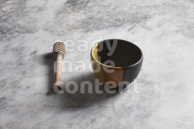 Multicolored pottery bowl with wooden honey dipper on the side on grey marble background