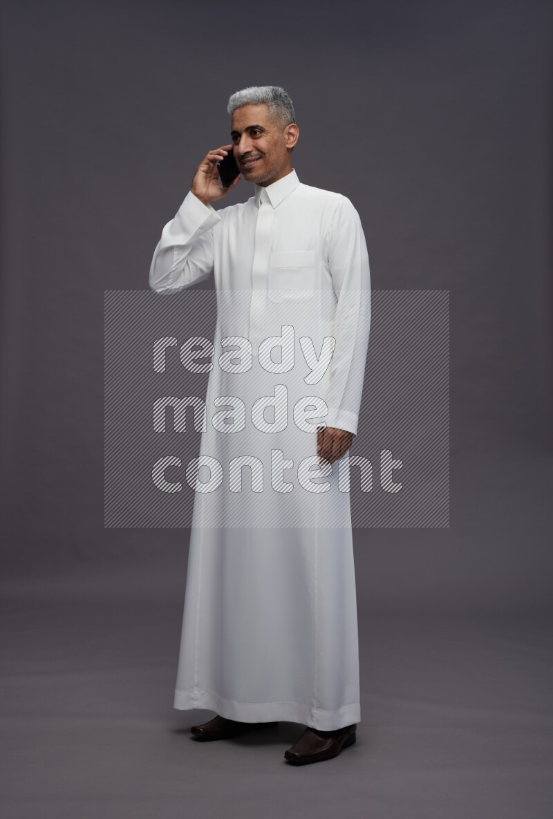 Saudi man wearing thob standing talking on phone on gray background