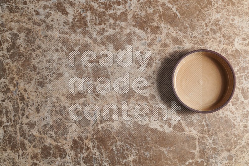 A beige pottery oven plate on beige marble background