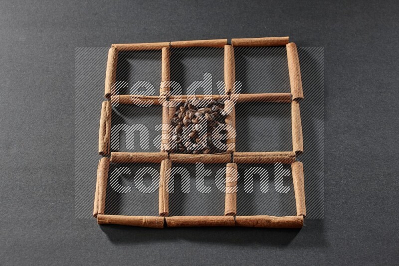 9 squares of cinnamon sticks full of coffee beans in the middle surrounded by nutmeg, dried mint, cloves, dried basil, dried ginger, cinnamon, star anise and cardamom on black flooring