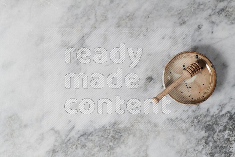 Multicolored pottery bowl with wooden honey dipper in it on grey marble background