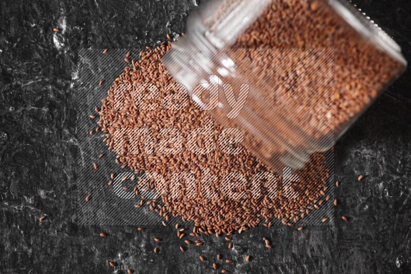 A glass jar full of garden cress seeds flipped and seeds spread out on a textured black flooring