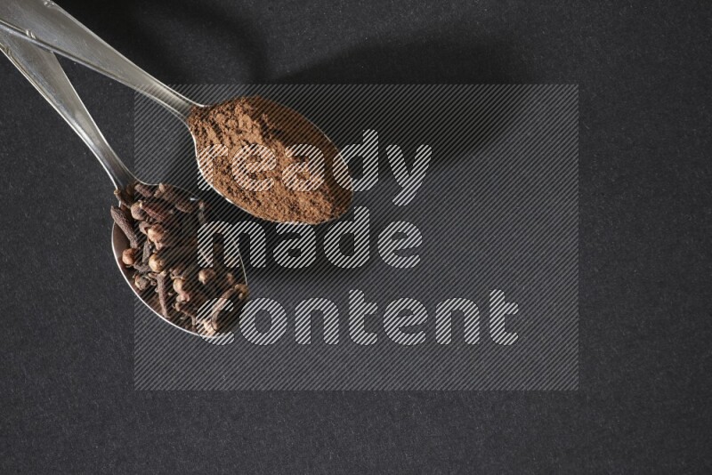 ملعقتان معدنيتان، إحداهما ممتلئة بحبوب القرنفل والأخرى ببودرة القرنفل، على خلفية سوداء