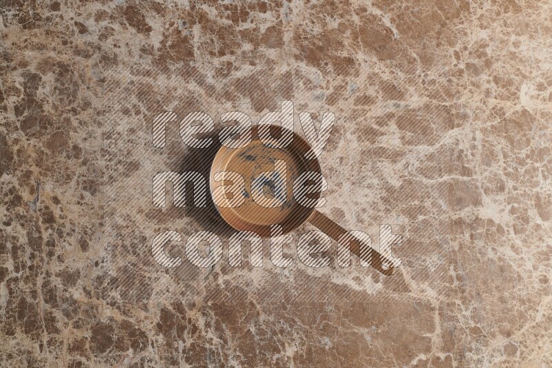 A small copper pan on beige marble background