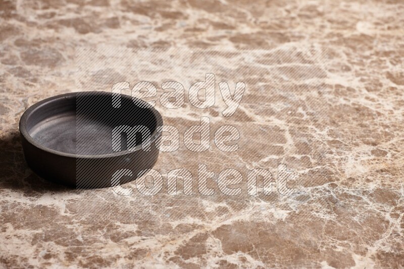 A black pottery bowl on beige marble background