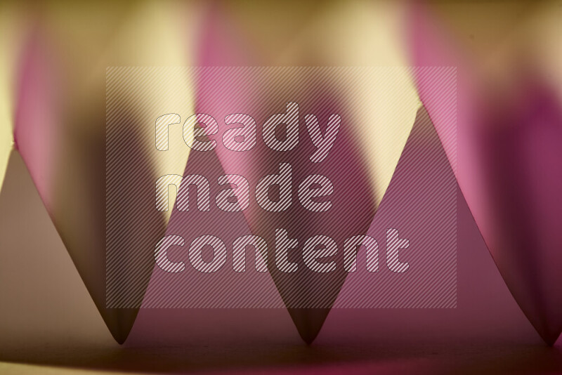 A close-up abstract image showing sharp geometric paper folds in pink gradients and warm tones