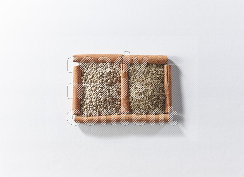 مربعان من أعواد القرفة ممتلئان بحبوب الفلفل الأبيض وحبوب الكمون علي خلفية بيضاء