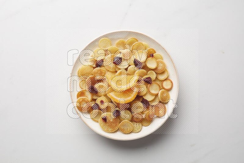 Top-view shot of orange candy cereal pancakes in a round bowl on white background