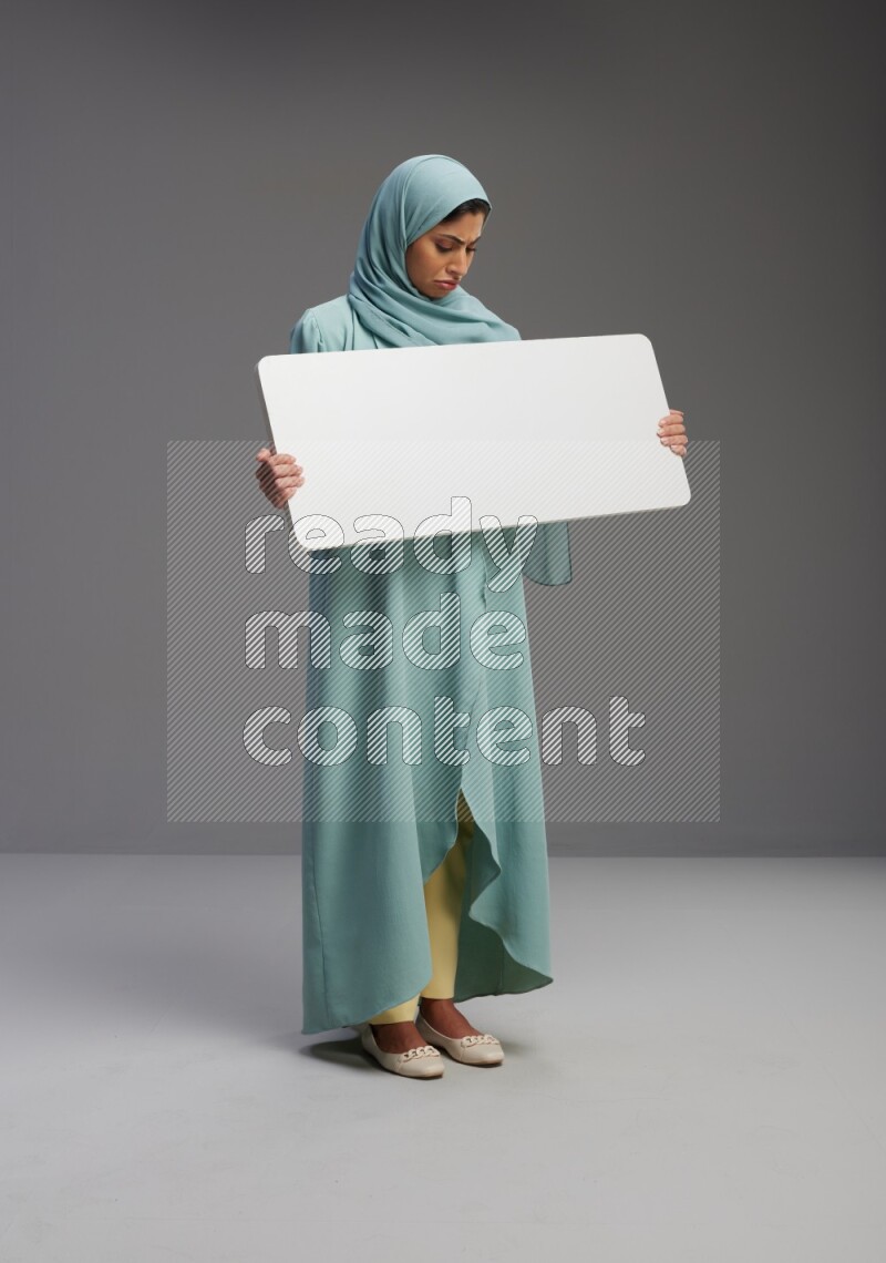 Saudi Woman wearing Abaya standing holding board on Gray background