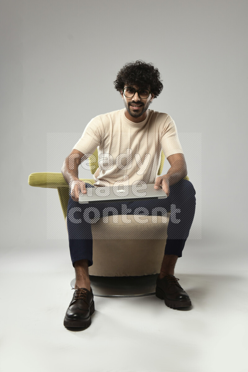 A man wearing casual sitting on a chair holding a laptop on white background