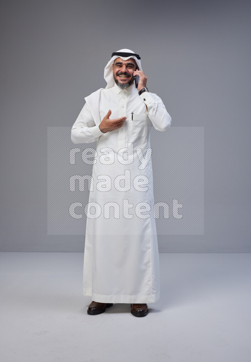 Saudi man Wearing Thob and white Shomag standing talking on phone on Gray background