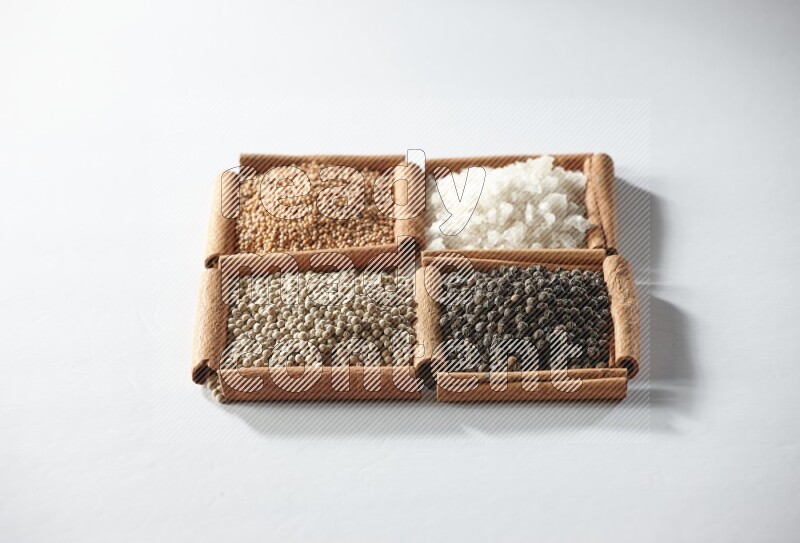 4 مربعات من أعواد القرفة ممتلئة بالخردل والملح والفلفل الأبيض والفلفل الأسود على أرضية بيضاء
