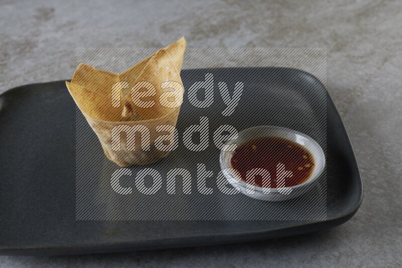 wonton cups with soy sauce ramkin on rectangle dark grey ceramic plate on grey textured counter top
