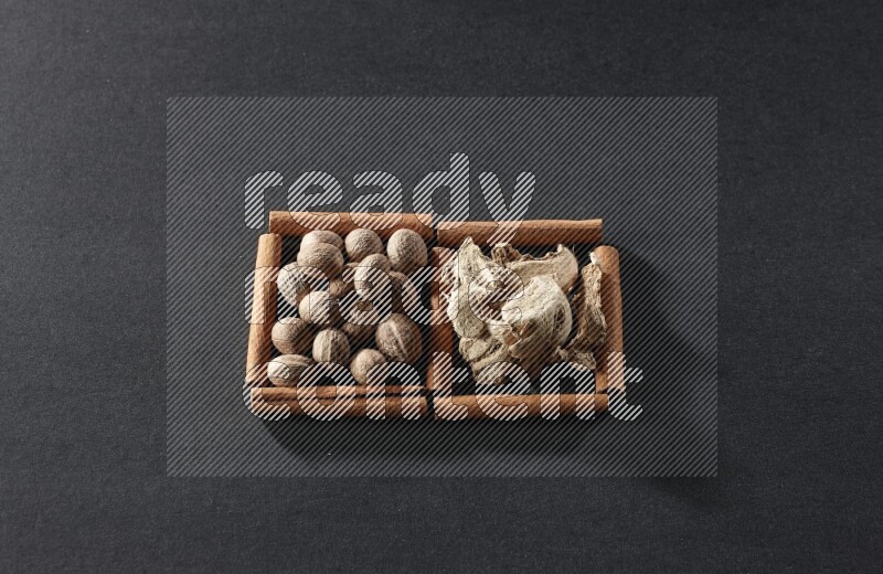 مربعان من أعواد القرفة ممتلئان بجوزة الطيب والزنجبيل المجفف علي خلفية سوداء