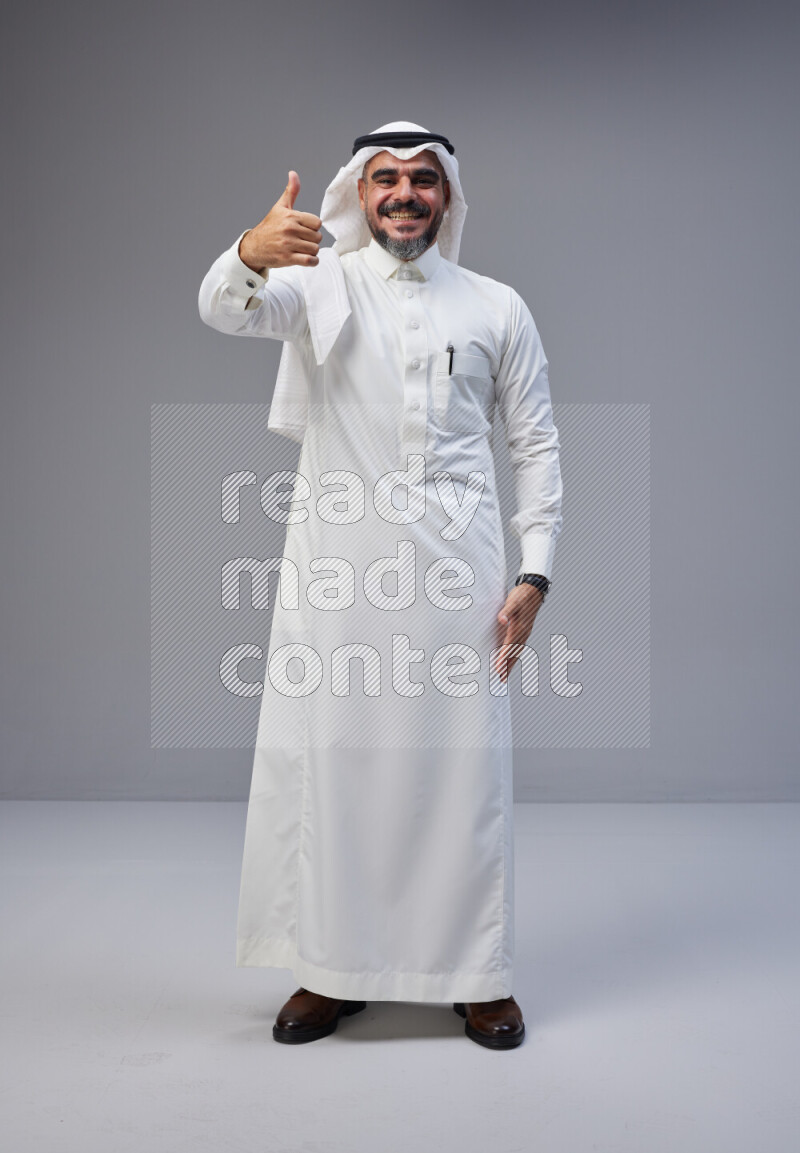 Saudi man Wearing Thob and white Shomag standing interacting with the camera on Gray background