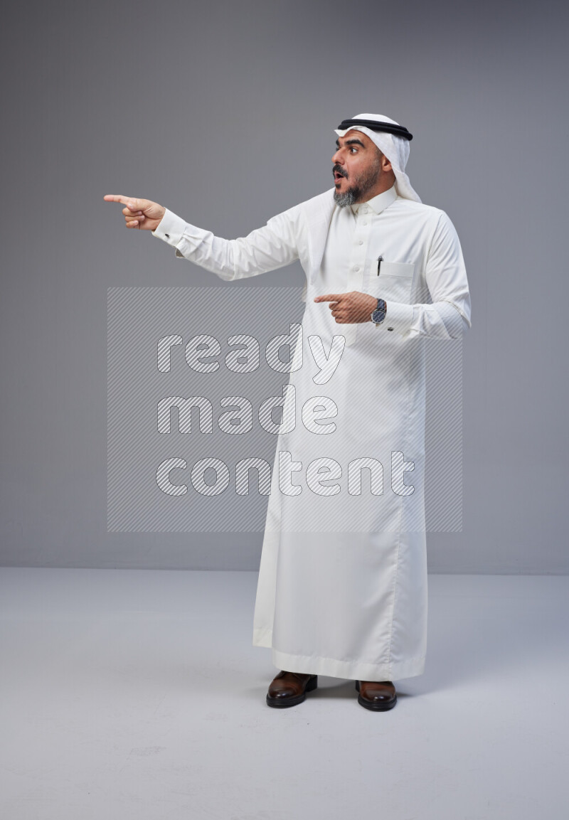 Saudi man Wearing Thob and white Shomag standing interacting with the camera on Gray background