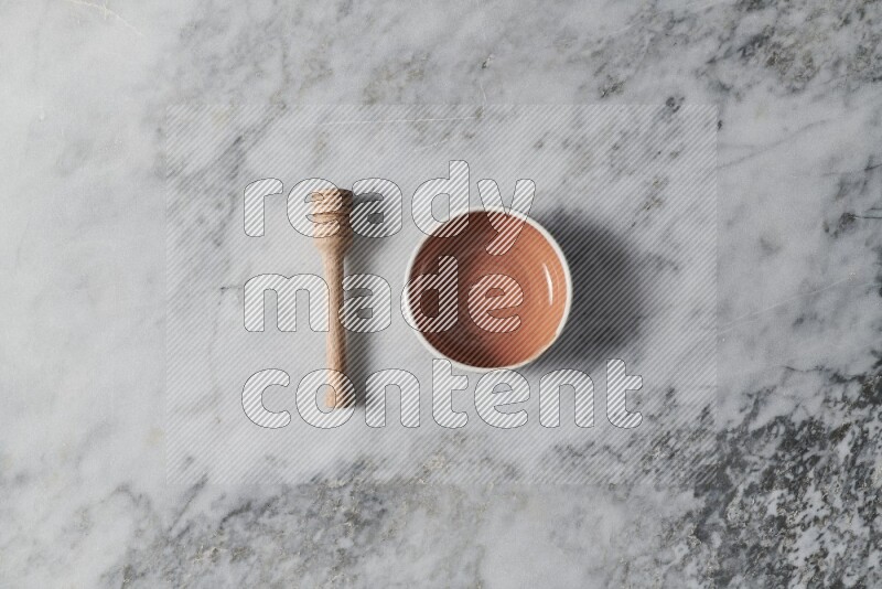 Brown pottery bowl with wooden honey dipper on the side on grey marble background