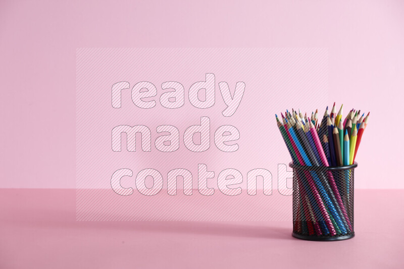 Pens, pencils and other different school supplies in a metal pen holder on rose background
