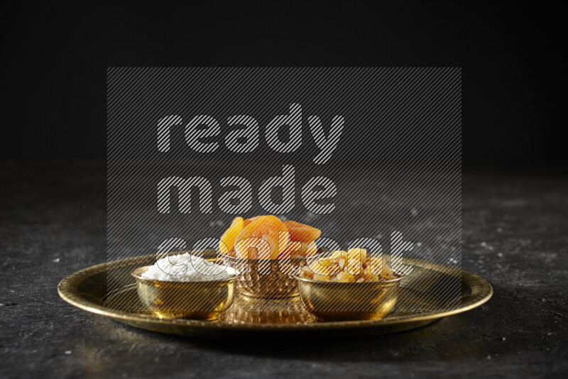 Dried fruits in metal bowls on a tray in a dark setup