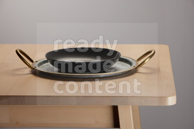 black plate placed on a rounded stainless steel metal tray with golden handels on the edge of wooden table