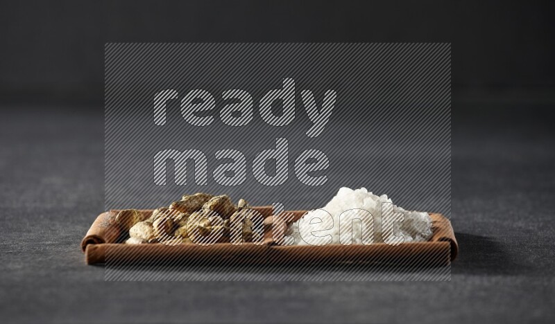 مربعان من أعواد القرفة ممتلئان بالملح الأبيض وأصابع الكركم علي خلفية سوداء