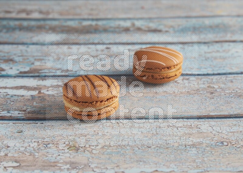 45º Shot of of two assorted Brown Irish Cream, and light brown Almond Cream macarons next to each other on light blue background
