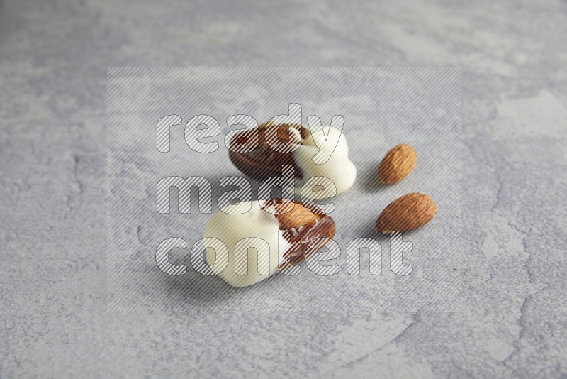 two almonds stuffed dates covered with white chololate with unroasted almonds on a light grey background