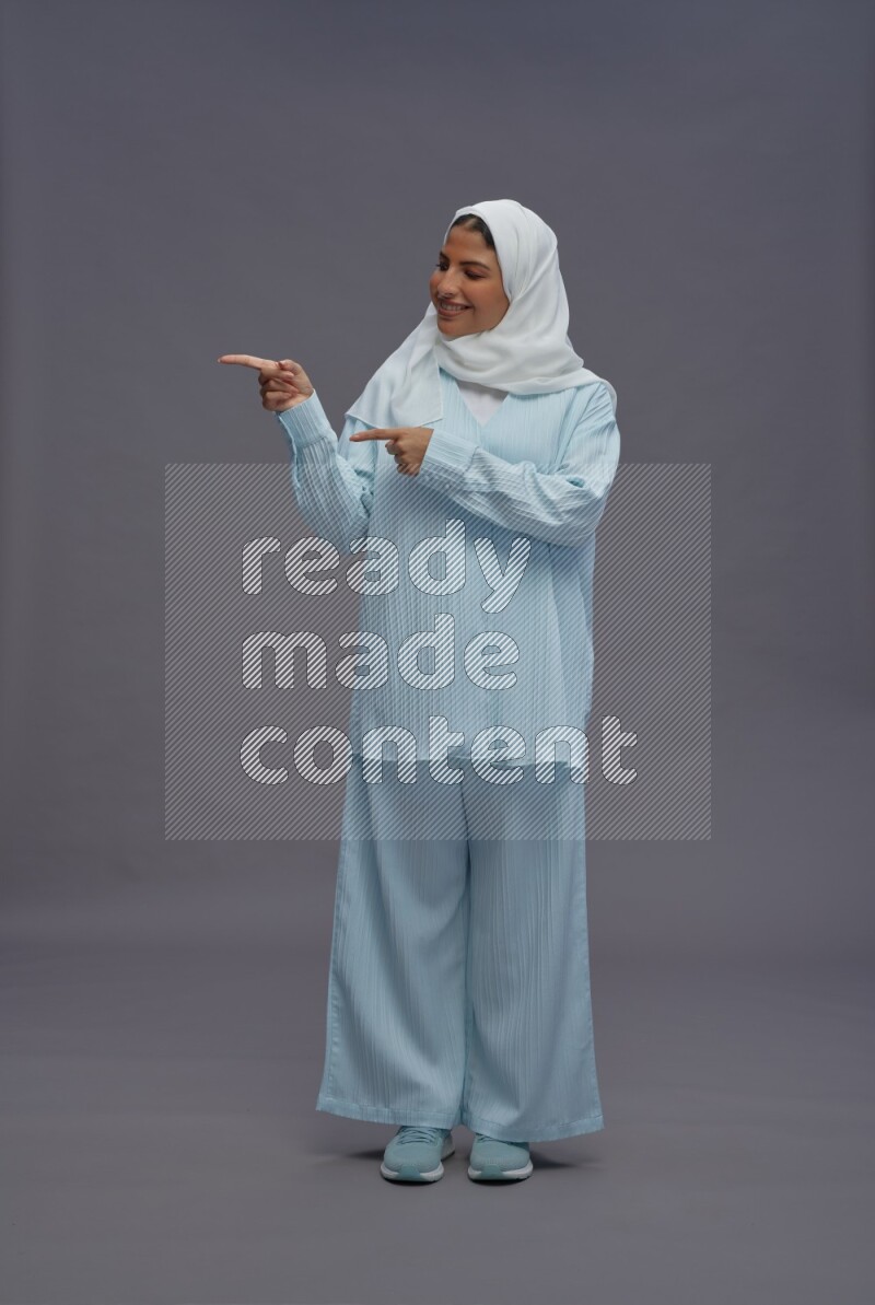 Saudi woman wearing hijab clothes standing interacting with the camera on gray background