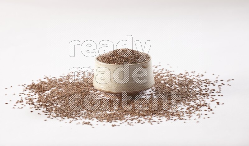 A pottery beige bowl full of flax seeds and more seeds spread on a white flooring