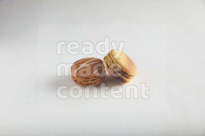 45º Shot of of two assorted Brown Irish Cream, and Yellow Crème Brulée macarons on white background