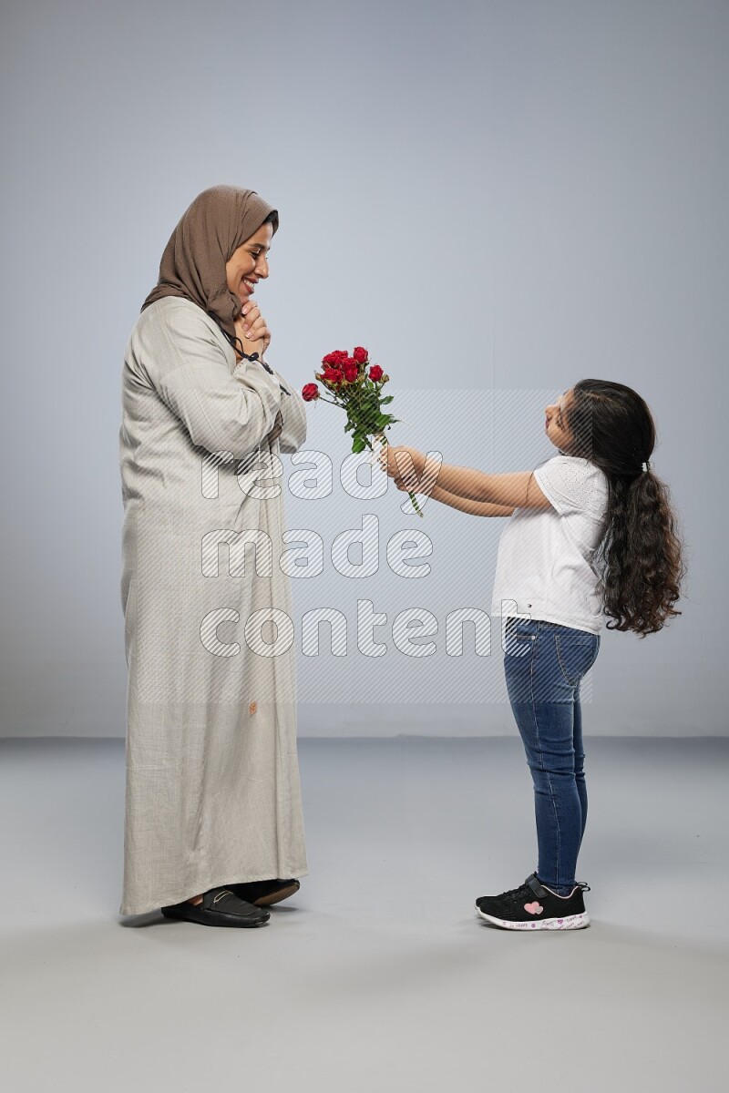 A girl standing giving flowers to her mother on gray background